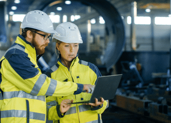 two construction workers pointing at a laptop in a manufacturing plant