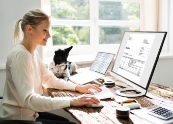 woman at home sitting at a desk smiling at a computer